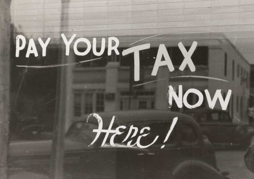 Photo from the 1900s of a store front window with the words "Pay Your Tax Now Here!"