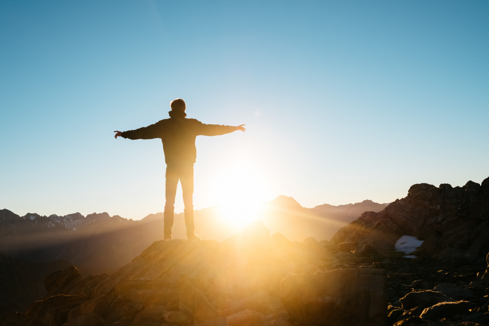 Person on top of hill with arms outstretched with sunrise in background