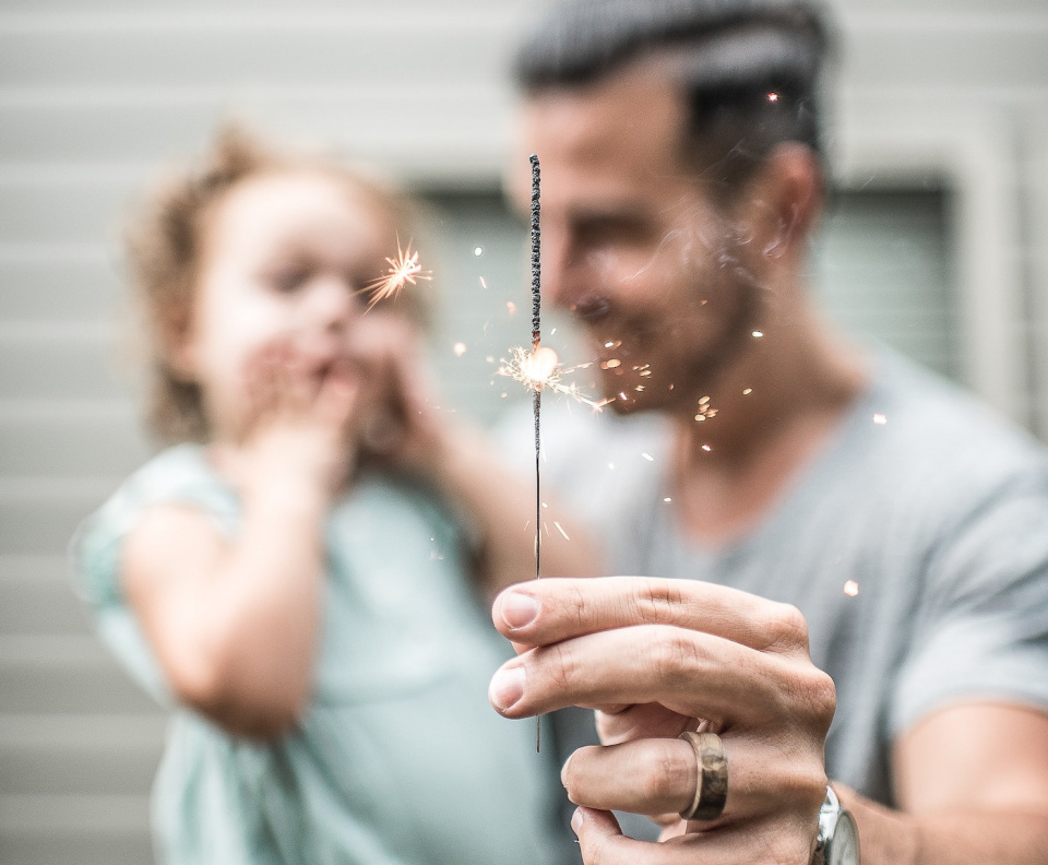 Man holding a sparkler firework toy while holding a child