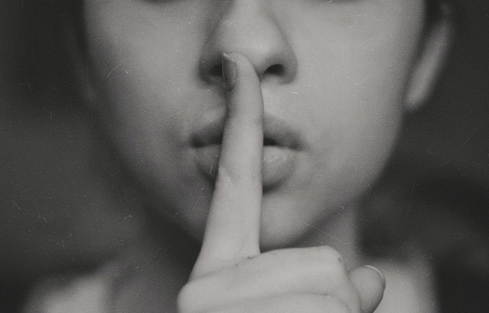 woman with a finger over her mouth making a "shh" sign