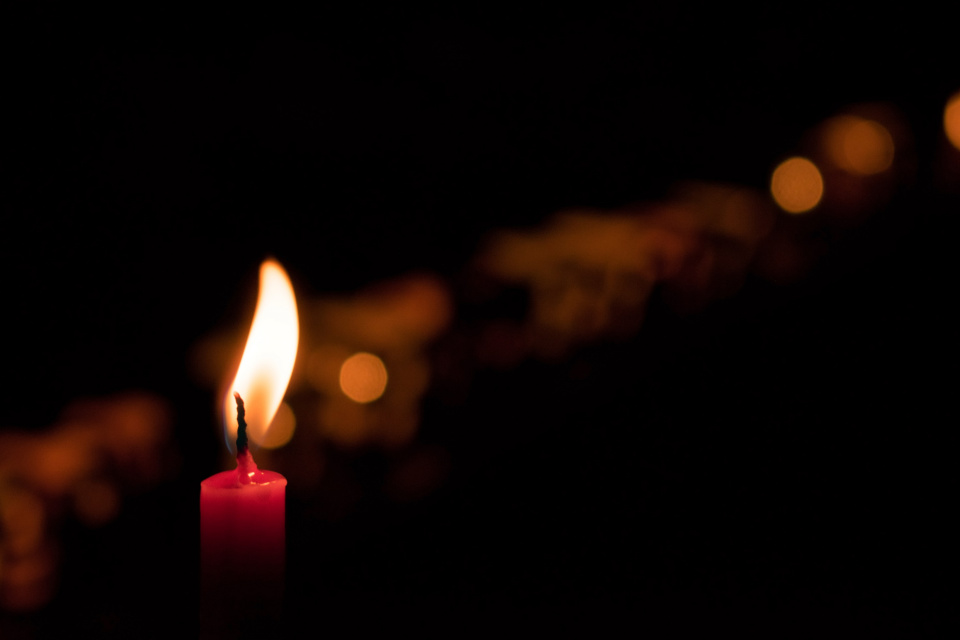 A red candle is seen in the foreground, in the background a long row of candles