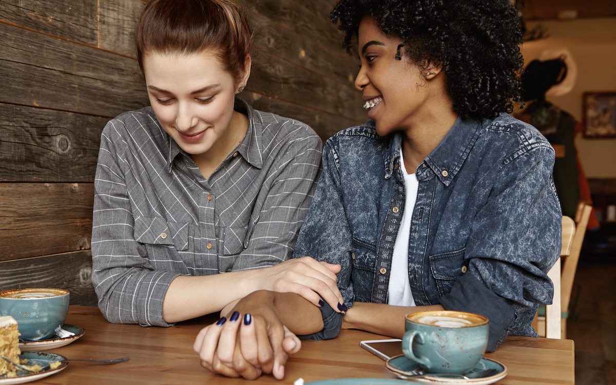 Queer 101: what do we mean when we say 'lesbian'? A picture of two lesbians holding hands in a cafe